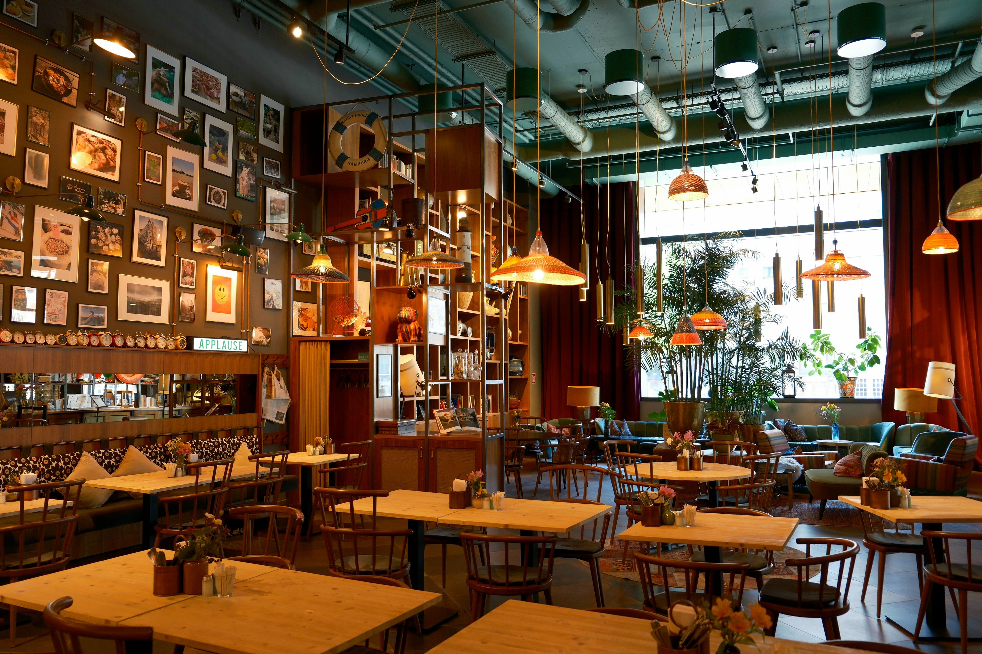 Een leeg restaurant met gedekte houten tafels en hanglampen, klaar voor de opening van de dag.