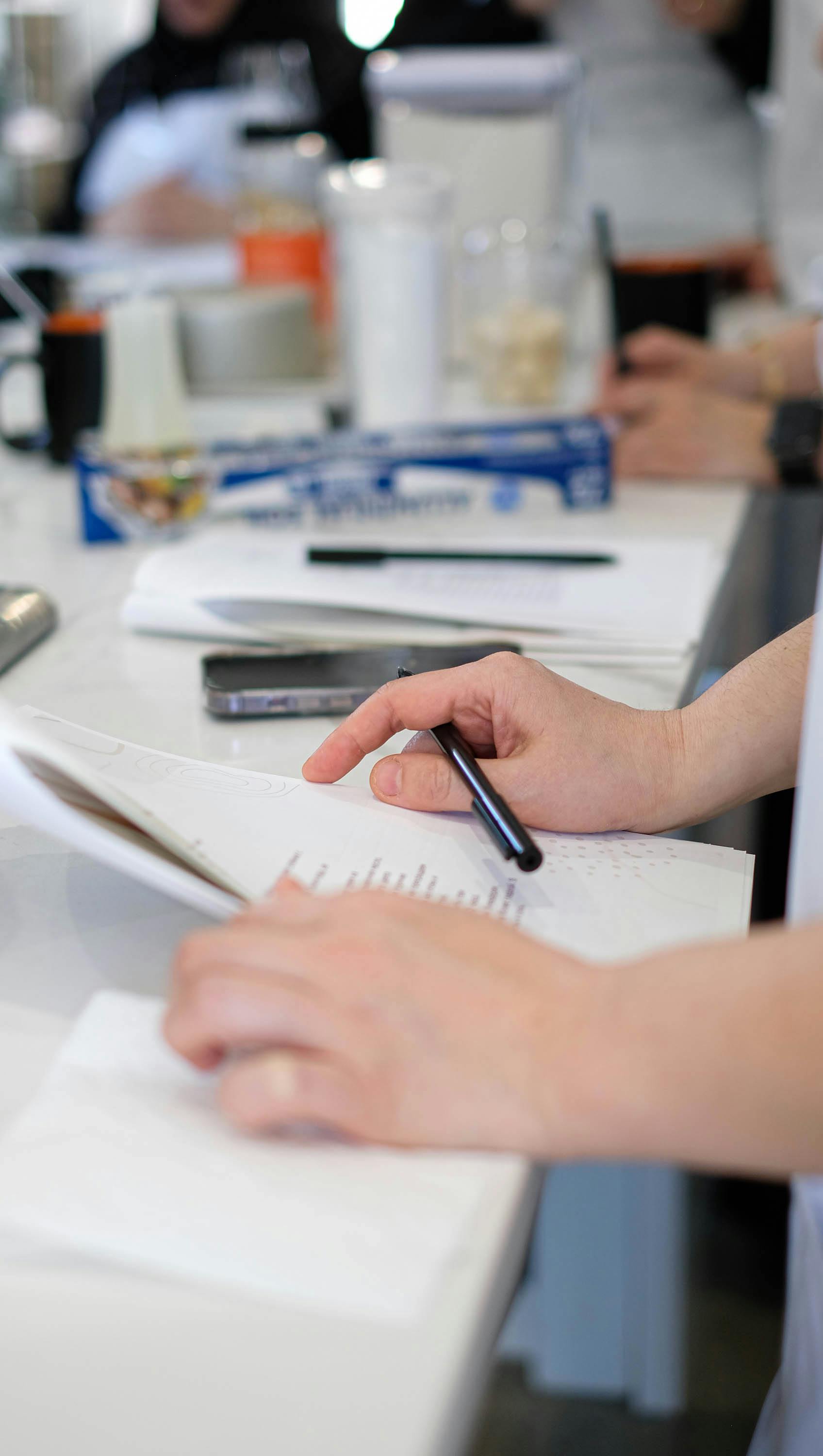 Someone filling in a list on paper with a pen at the kitchen counter, a phone lying beside it.