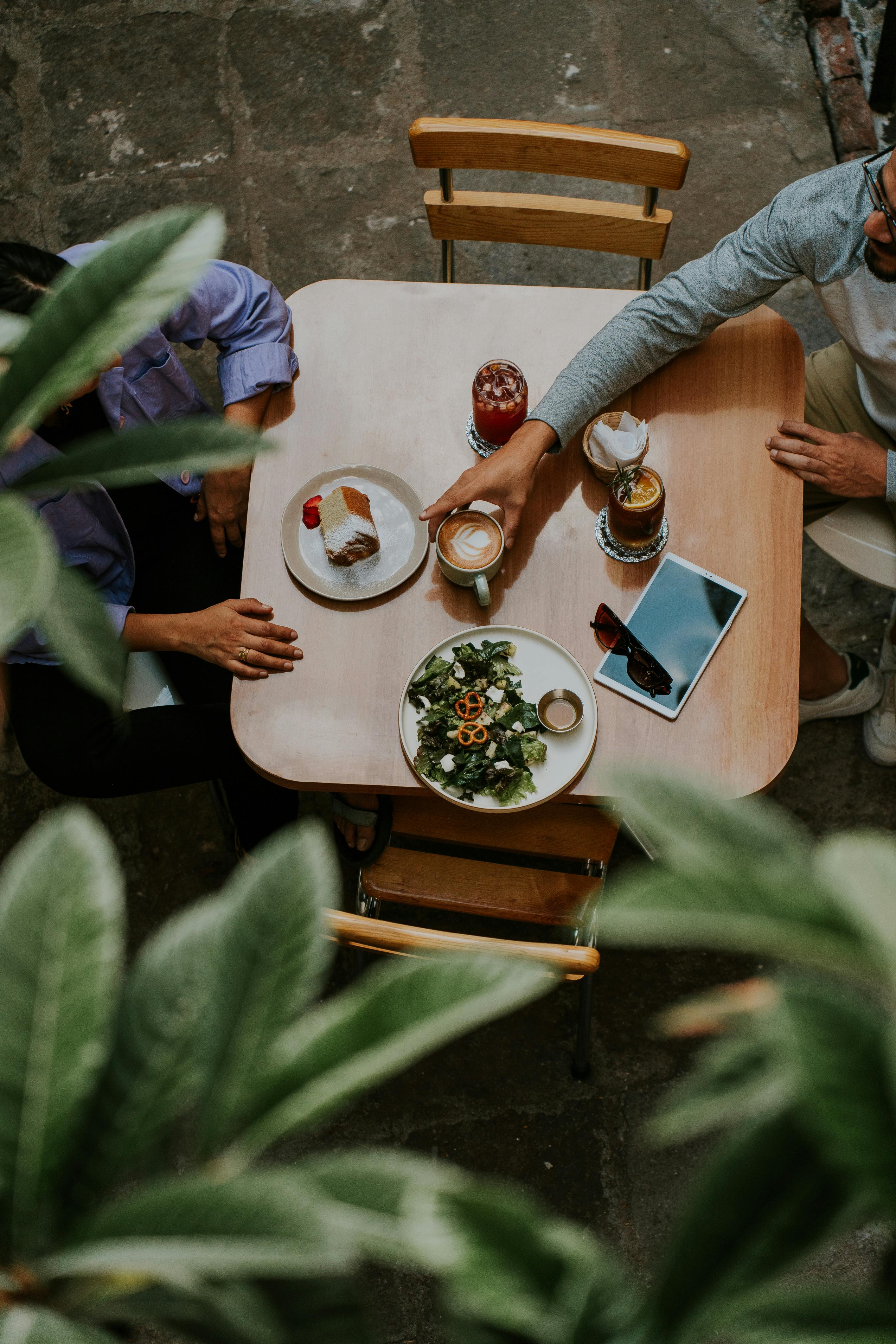 Seen from above, two people at a terrace table with coffee, a salad and a tablet, a day off the way it is meant to be.