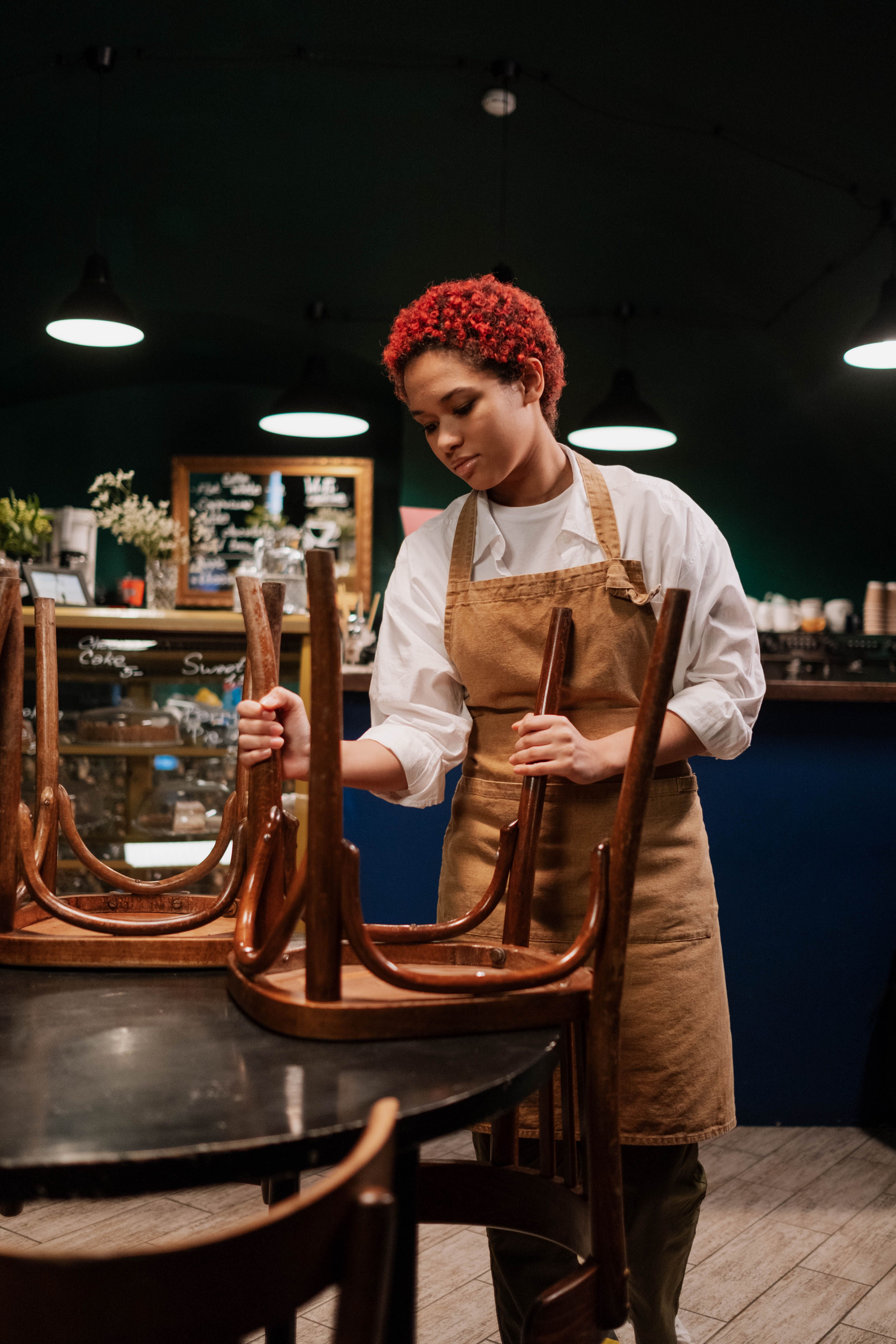 A staff member in an apron setting up chairs at the start of the shift in an empty café.