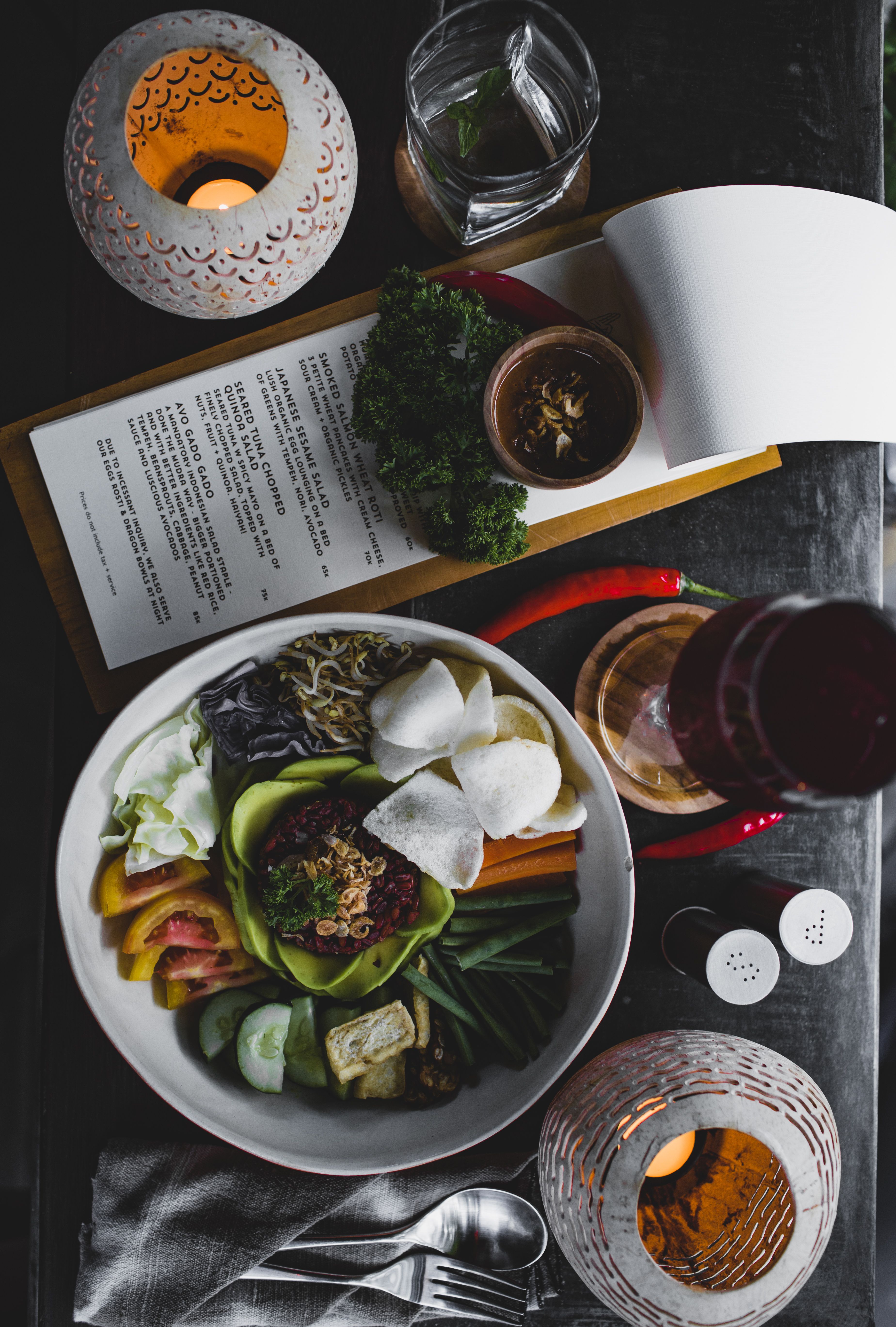 Seen from above, a menu card on a wooden board next to a plate of vegetables, the place where a guest expects to find allergen information.